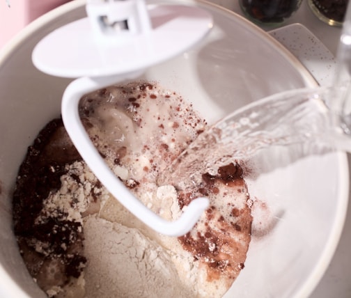 Person adding bread ingredients to stand mixer bowl Person adding bread ingredients to stand mixer bowl