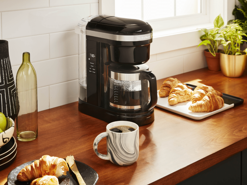 KitchenAid® coffee maker on countertop with croissants and mug of coffee KitchenAid® coffee maker on countertop with croissants and mug of coffee