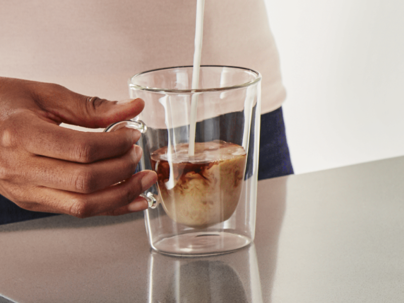 Milk being poured into glass cup of coffee