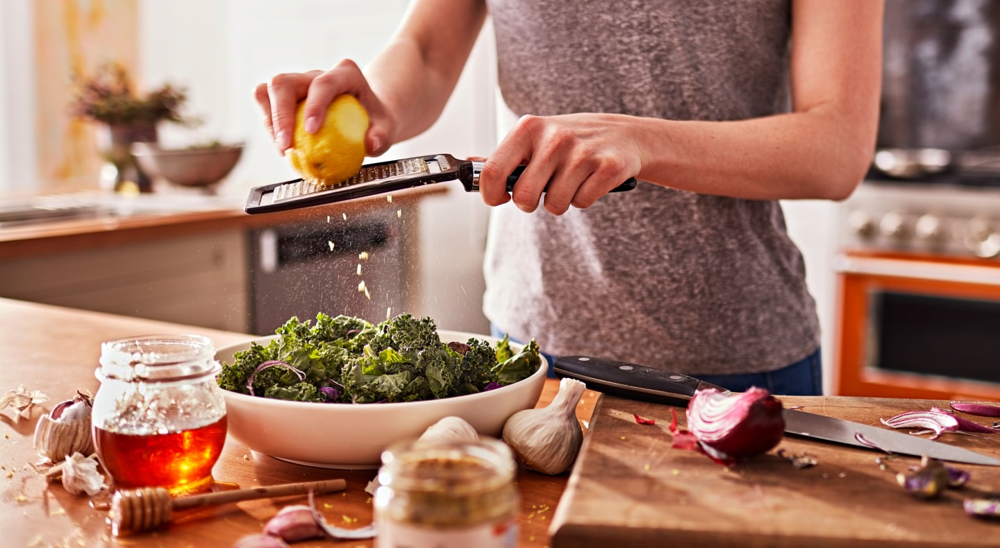 A woman shredding lemon peel onto a chopped salad in a modern kitchen. A woman shredding lemon peel onto a chopped salad in a modern kitchen.