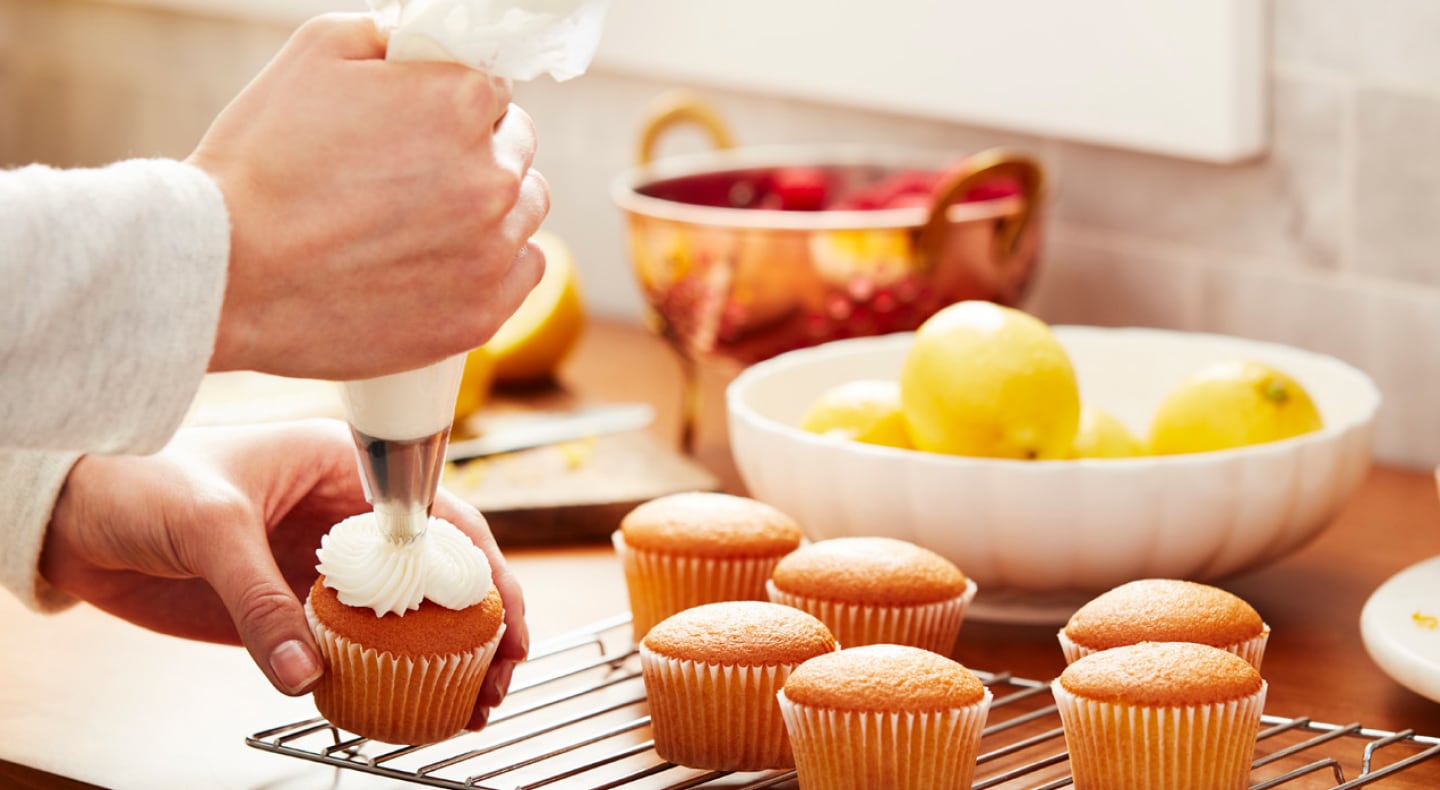 Vanilla cupcakes being frosted with cream cheese frosting Vanilla cupcakes being frosted with cream cheese frosting