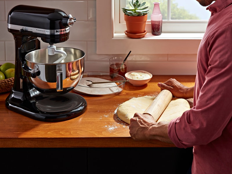 Person rolling out dough next to a black KitchenAid® stand mixer Person rolling out dough next to a black KitchenAid® stand mixer