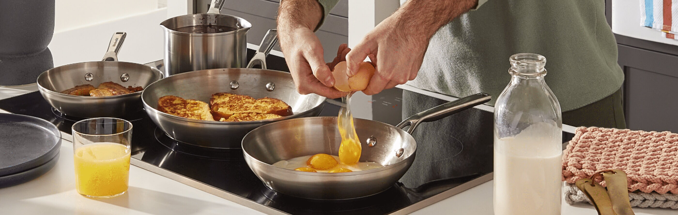 Eggs being cracked into a pan on the stove along with other items on the cooktop