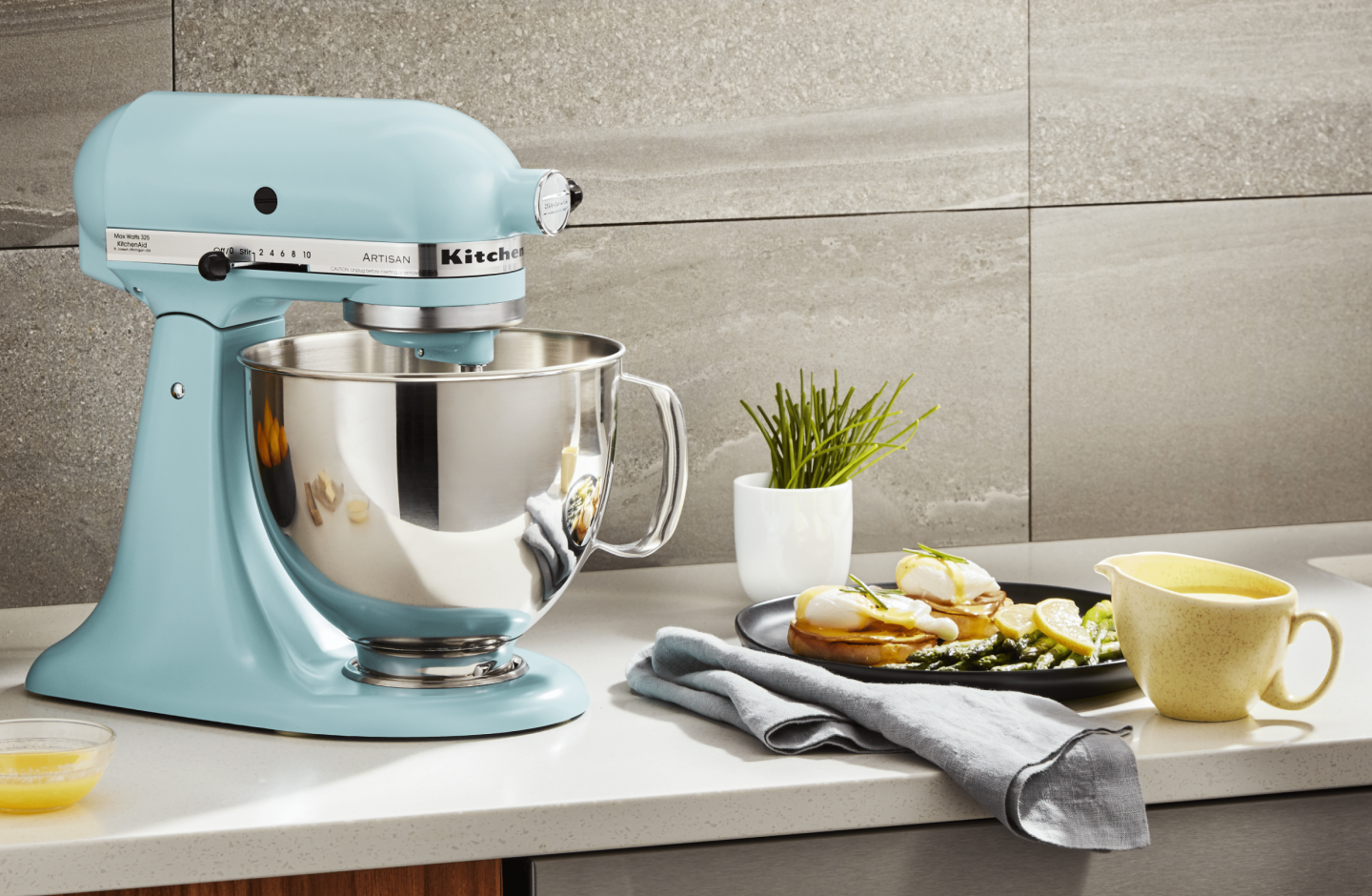 A stand mixer sitting next to a plate of eggs benedict A stand mixer sitting next to a plate of eggs benedict