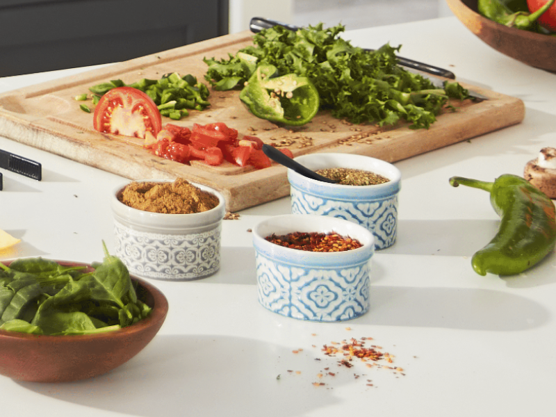Chopped tomato and peppers on cutting board next to bowls of spices
