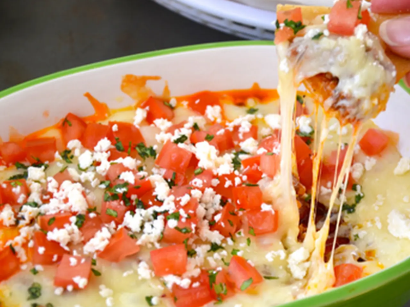 Person dipping chips into bowl homemade queso with fresh tomatoes on top