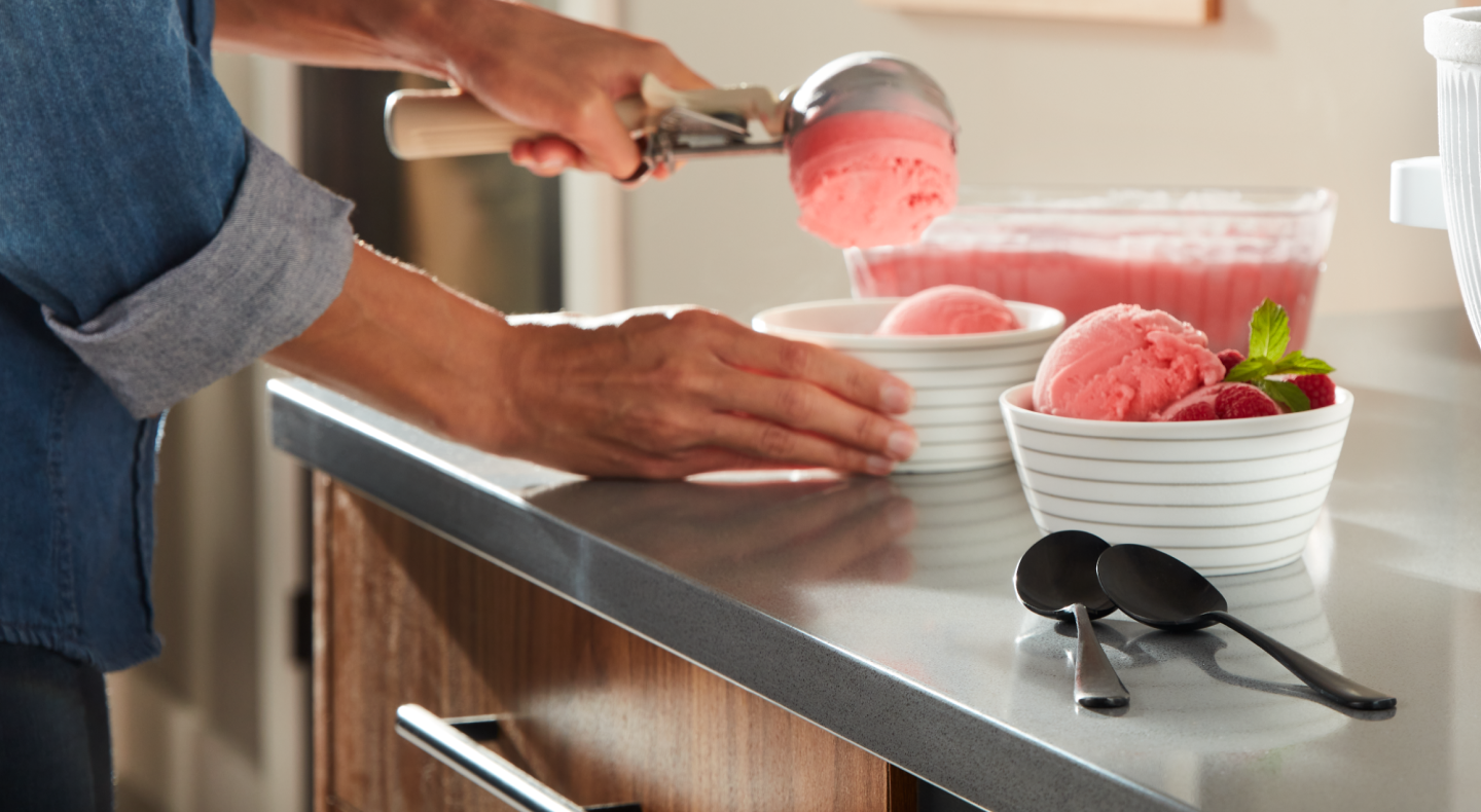 A person scooping strawberry ice cream into dishes. A person scooping strawberry ice cream into dishes.