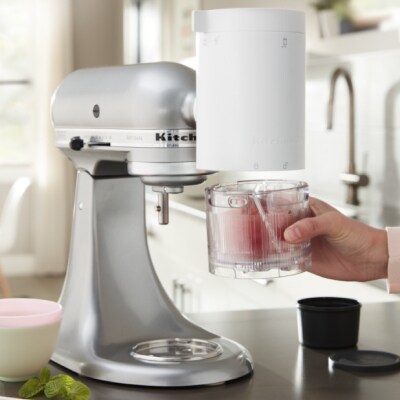 Hand holding a glass cup under a KitchenAid® Stand Mixer with Shave Ice Attachment