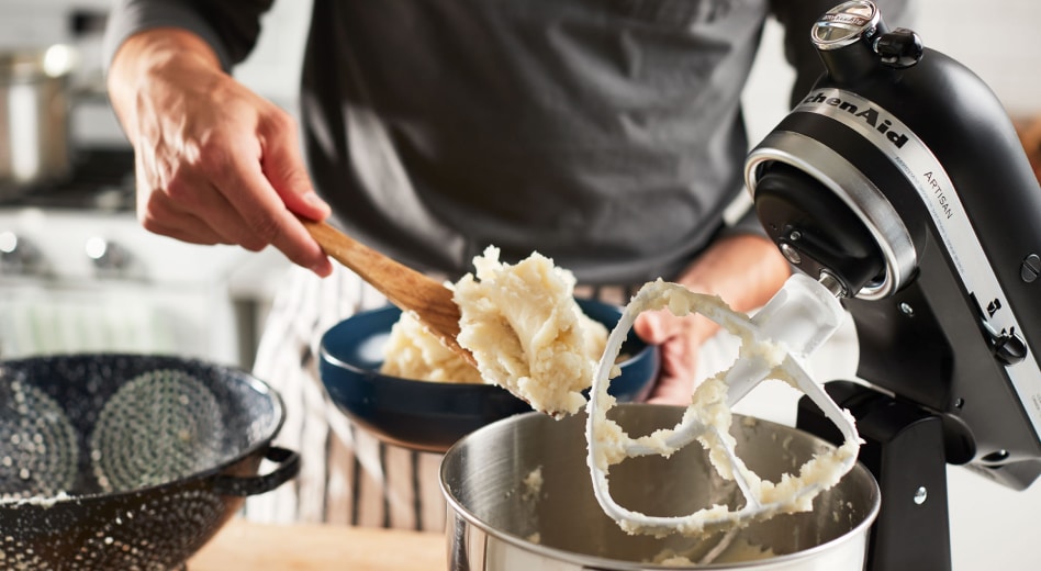 Man scooping mashed potatoes out of a stand mixer with paddle Man scooping mashed potatoes out of a stand mixer with paddle