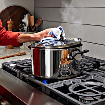 Hand lifting lid from large pot on cooktop