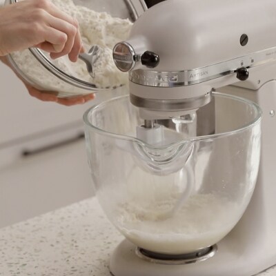 A person adding dough ingredients to a mixer