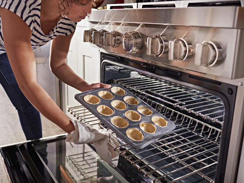Person loading miniature pie shells in a muffin tin into the oven