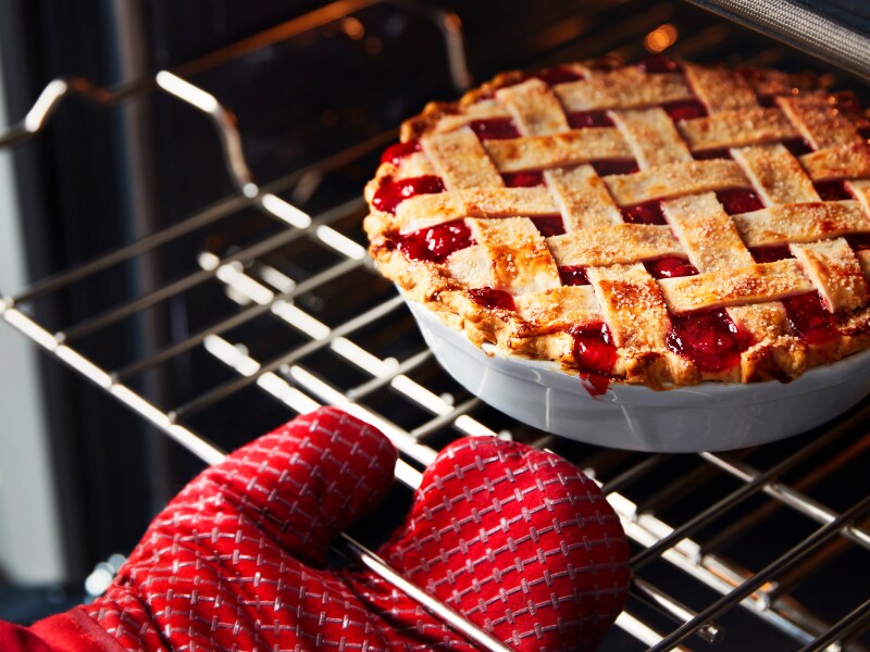 Person with a red oven mitt pulling a cherry pie out of the oven