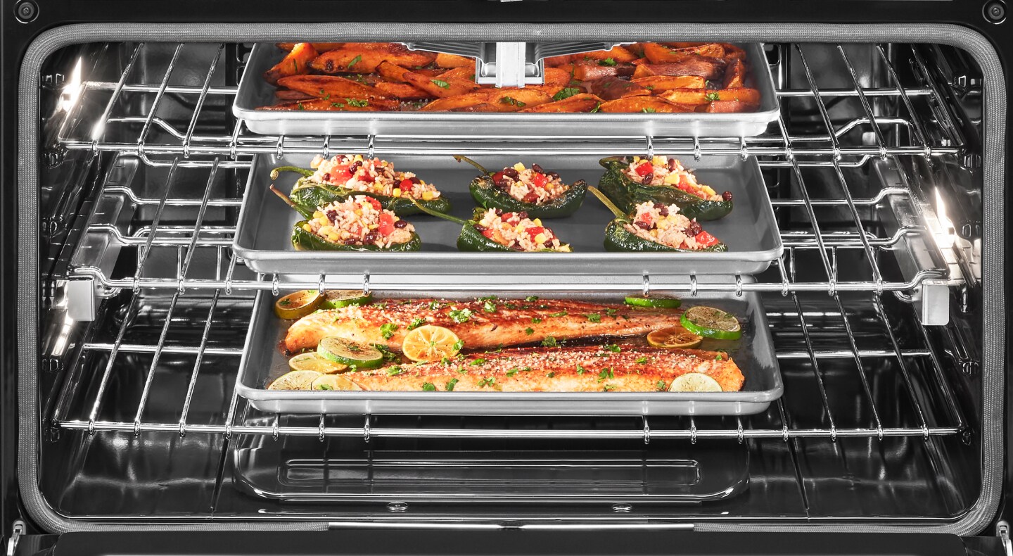 Open oven cavity with three pans roasting fish and vegetables inside Open oven cavity with three pans roasting fish and vegetables inside