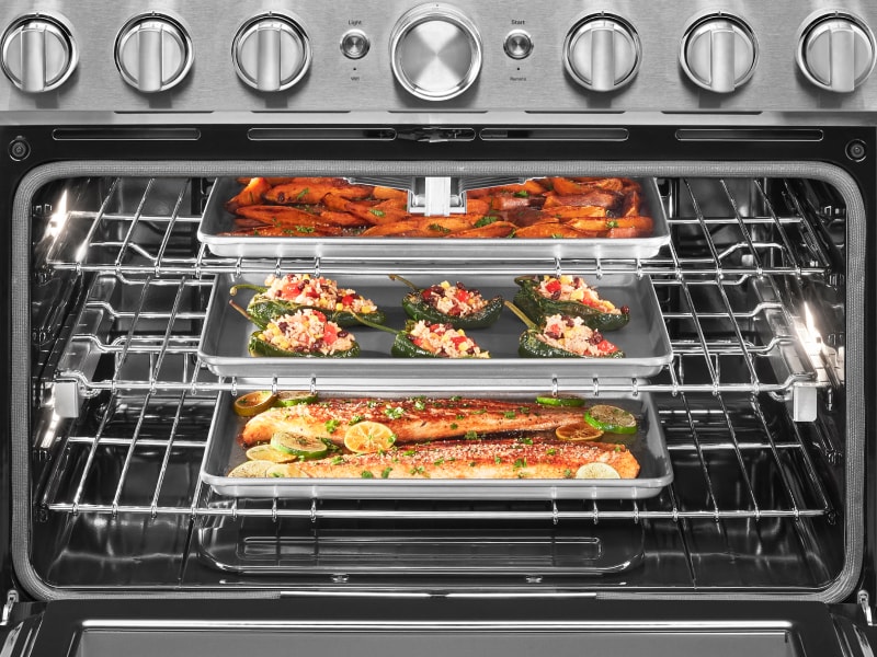 Open oven cavity with three pans roasting fish and vegetables inside Open oven cavity with three pans roasting fish and vegetables inside