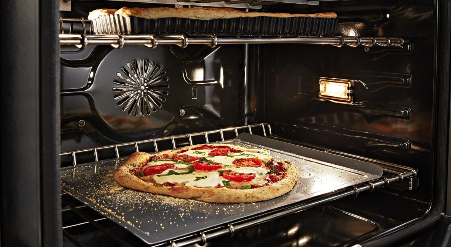 Artisan pizza baking in a convection oven with a dish baking on the rack above Artisan pizza baking in a convection oven with a dish baking on the rack above
