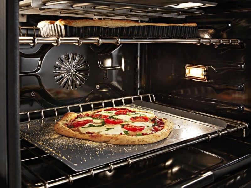Artisan pizza baking in a convection oven with a dish baking on the rack above Artisan pizza baking in a convection oven with a dish baking on the rack above