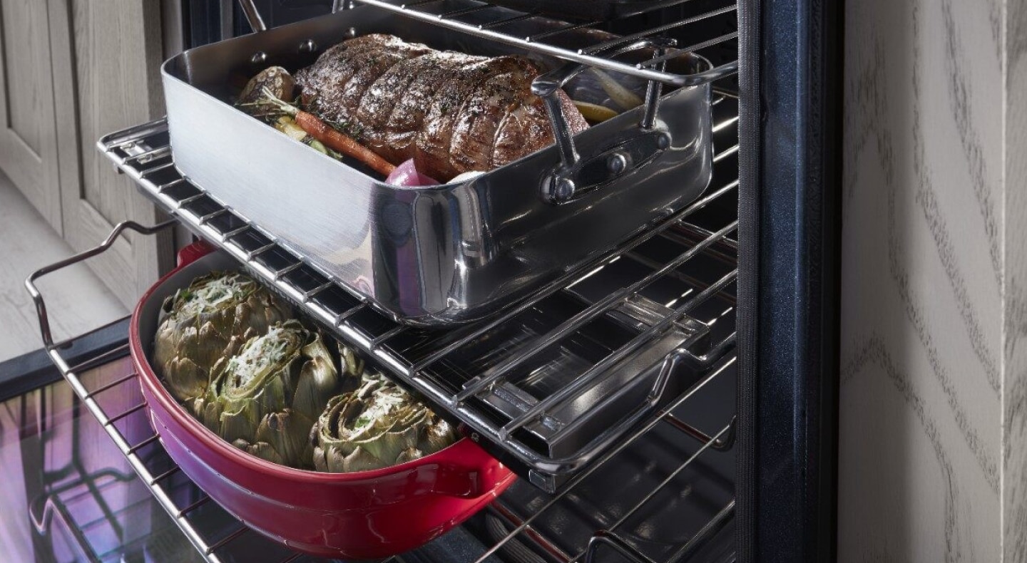 Close-up of two large meat and vegetable dishes sitting on top of extended bottom and top oven racks Close-up of two large meat and vegetable dishes sitting on top of extended bottom and top oven racks