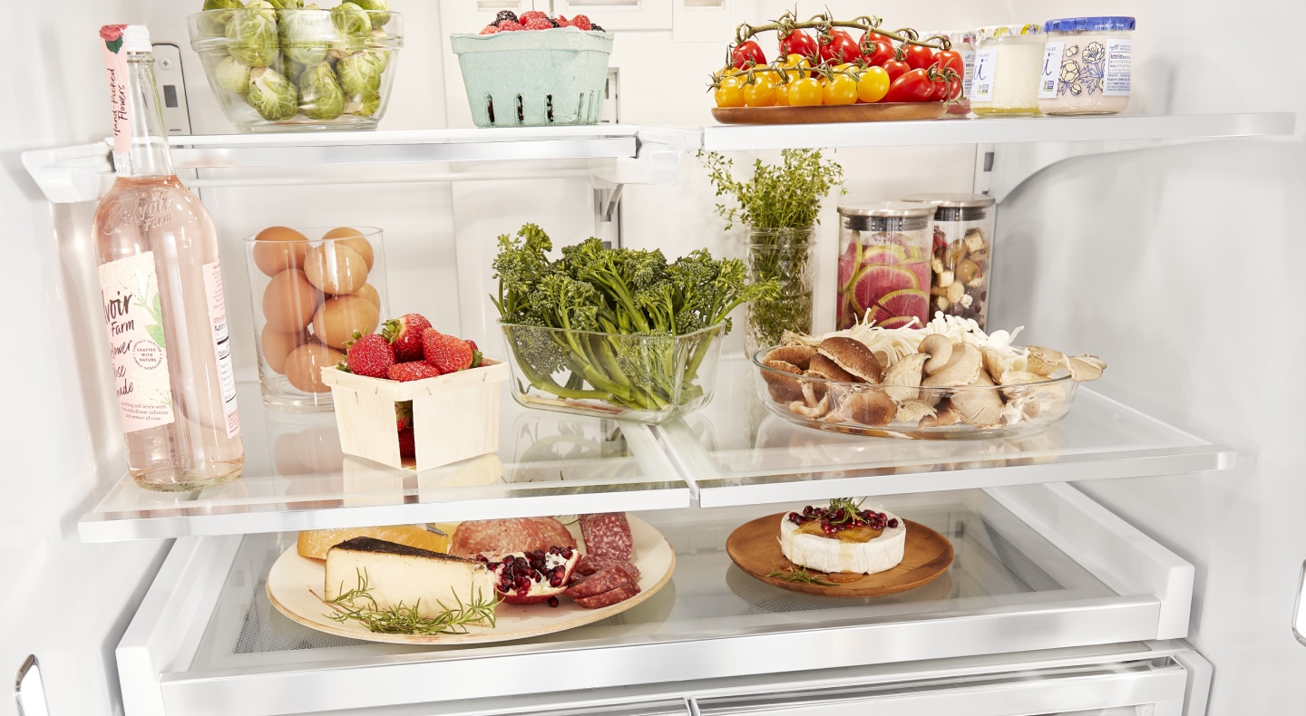 A charcuterie plate, herbs, fruits and vegetables organized on fridge shelves. A charcuterie plate, herbs, fruits and vegetables organized on fridge shelves.