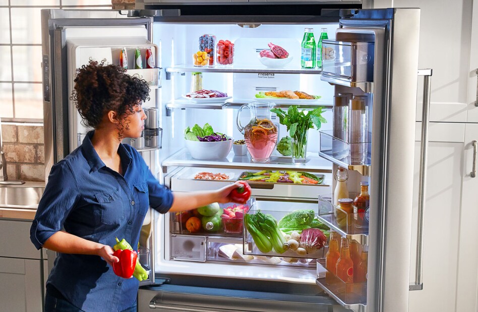 A woman placing a red pepper into an opened crisper drawer. A woman placing a red pepper into an opened crisper drawer.