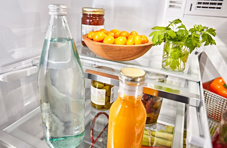 A red jar, bottled drinks and produce resting on refrigerator shelves. A red jar, bottled drinks and produce resting on refrigerator shelves.