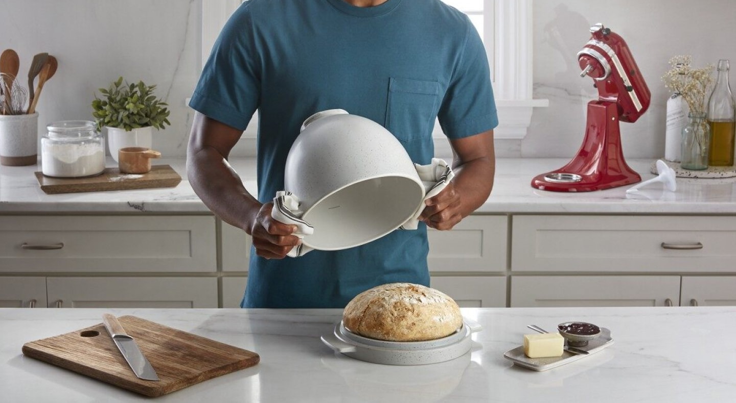 Person removing a bread proofing bowl from a baked bread loaf