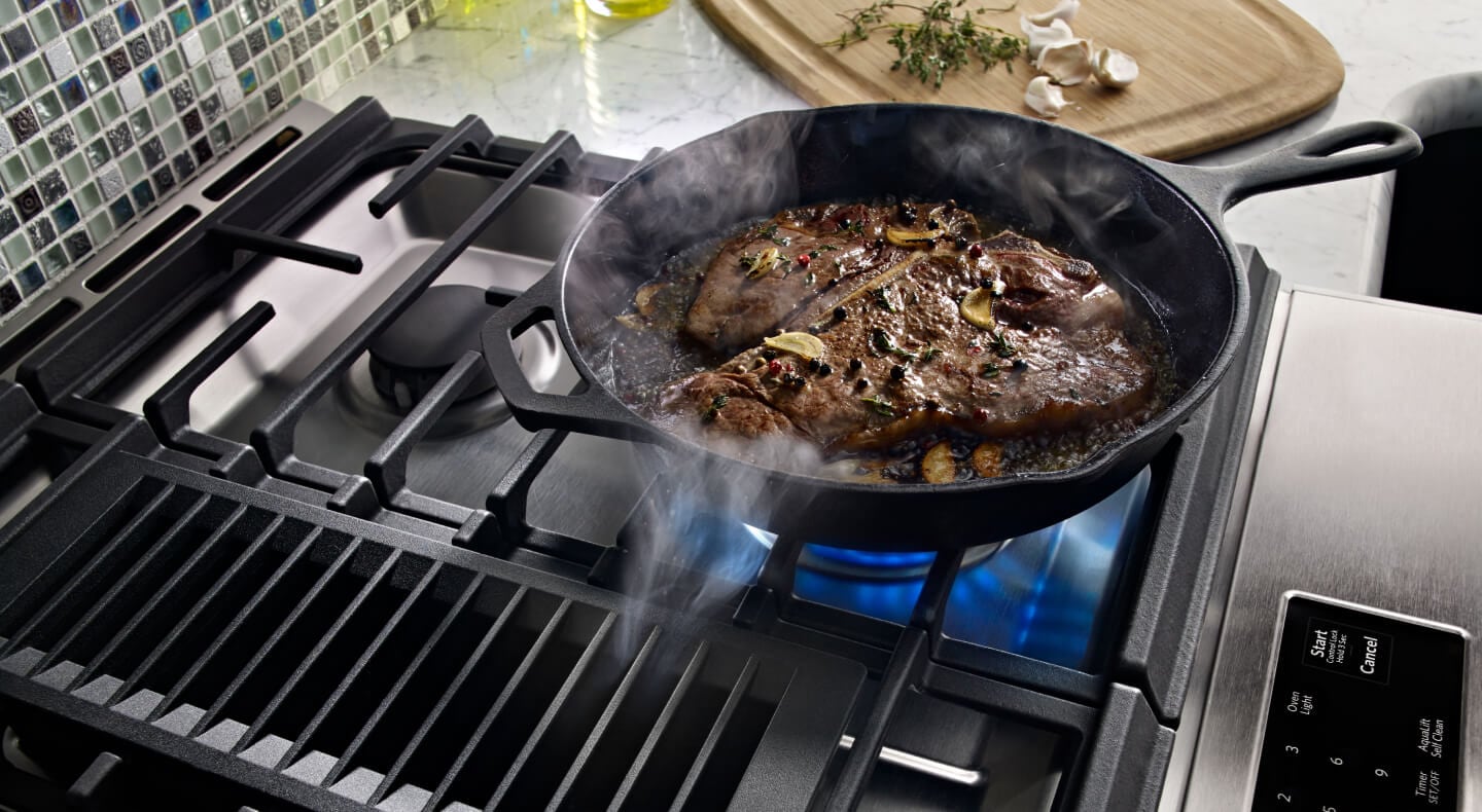 A garnished t-bone steak cooking in a cast iron skillet