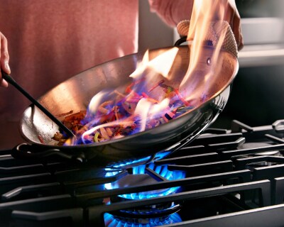 Hands cooking a flambe dish in a skillet over a gas stovetop
