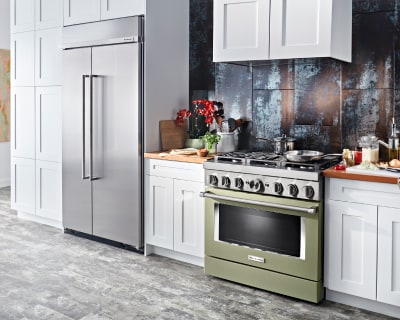 Kitchen with olive green stove, white cabinetry and french door refrigerator with ingredients on countertop