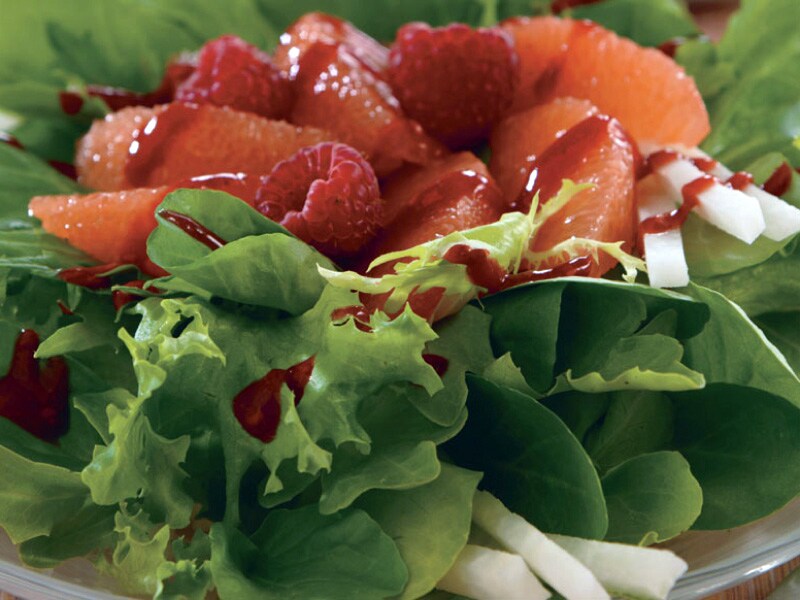 Close-up of raspberries and grapefruit topping shredded greens 