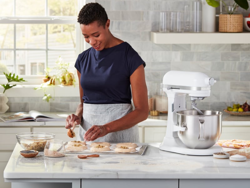 Person sprinkling herbs and seeds on top of shaped bagel dough Person sprinkling herbs and seeds on top of shaped bagel dough