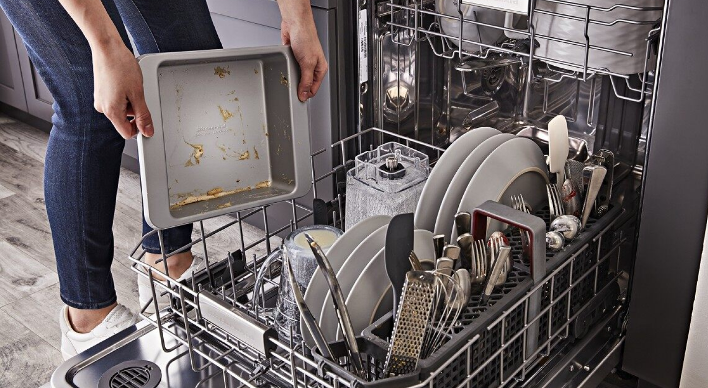 A person loading a dirty pan into the bottom rack of a KitchenAid® dishwasher A person loading a dirty pan into the bottom rack of a KitchenAid® dishwasher