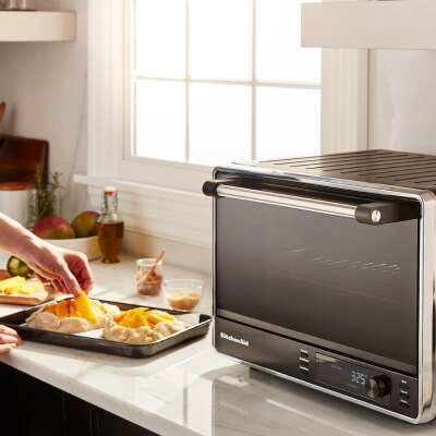 A person preheating a black KitchenAid® countertop oven to make pastries