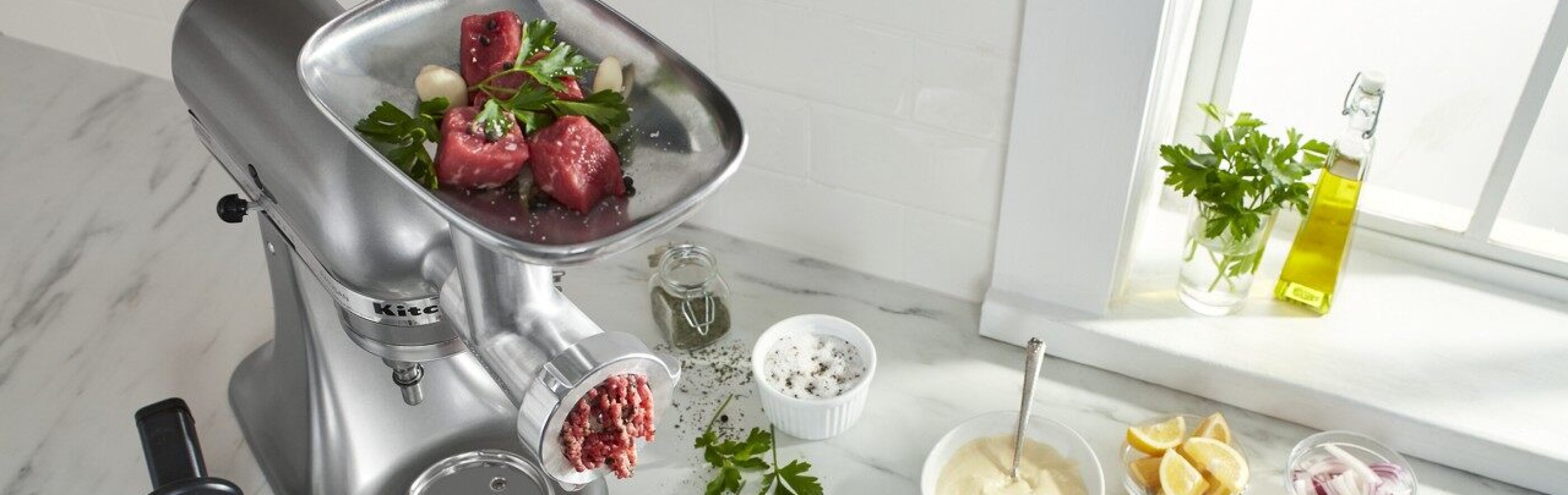 KitchenAid® Stand Mixer with food grinder attachment grinding meat on counter with ingredients