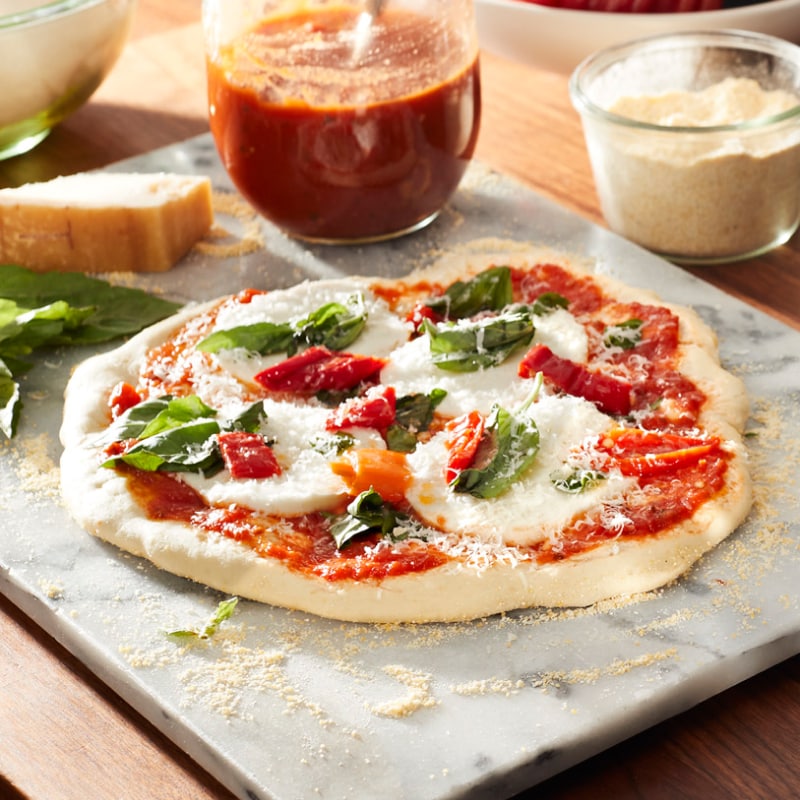 Homemade pizza on granite board surrounded by ingredients.