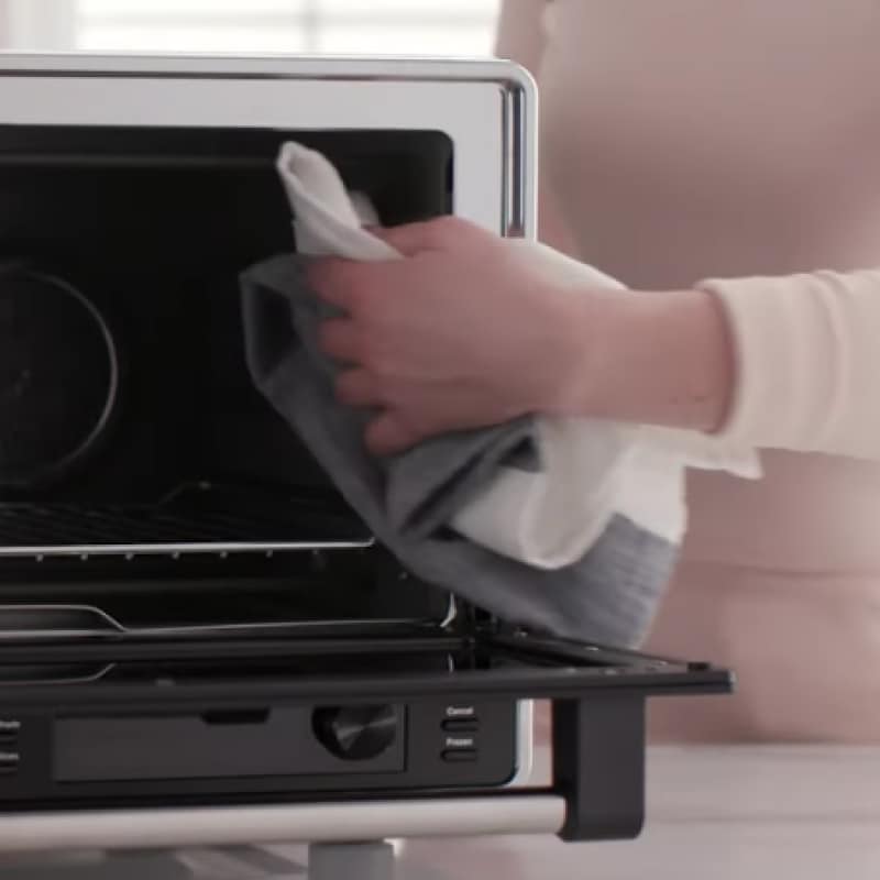 Person cleaning inside of air fryer with cloth.