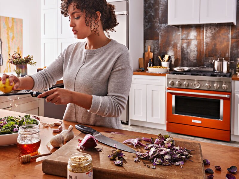 Person grating lemon over a salad with a KitchenAid® range behind them Person grating lemon over a salad with a KitchenAid® range behind them