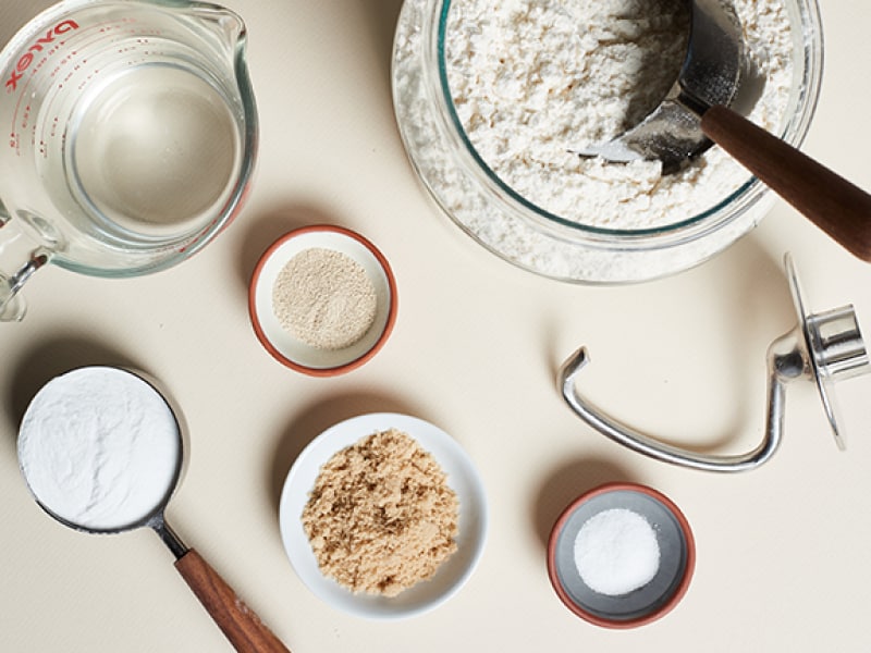 Dough ingredients and measuring cups next to a dough hook Dough ingredients and measuring cups next to a dough hook
