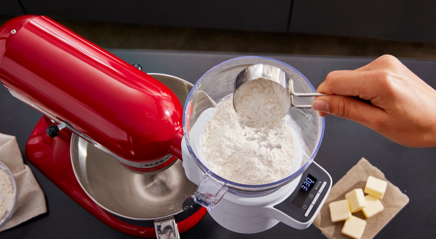 Person pouring flour from a measuring cup into the KitchenAid® Sifter + Scale Attachment
