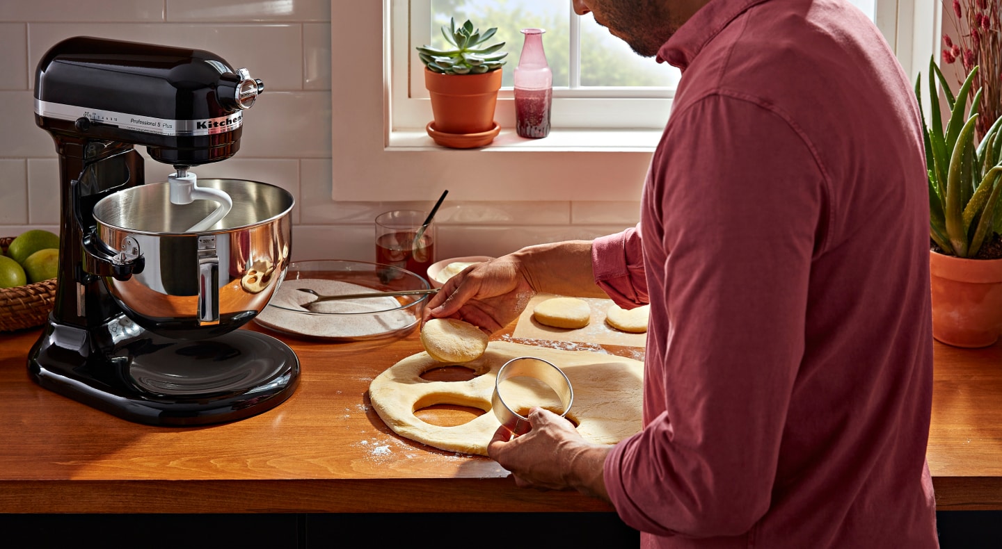 Person using a biscuit cutter to cut biscuit shapes into bread dough Person using a biscuit cutter to cut biscuit shapes into bread dough