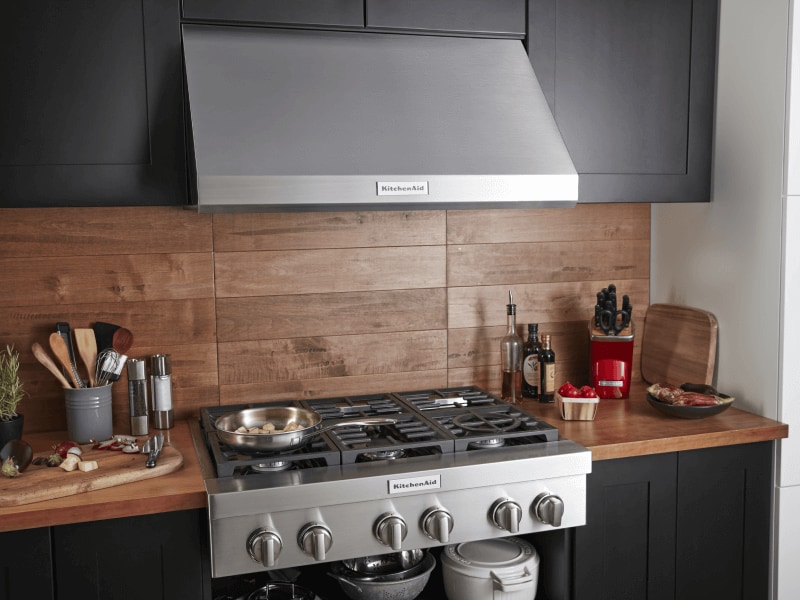 Stainless steel gas range and range hood set into a wooden countertop and backsplash