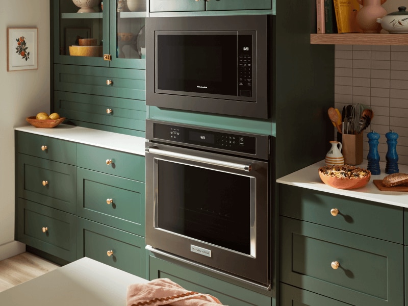Stainless steel wall oven and black microwave set into deep green cabinetry