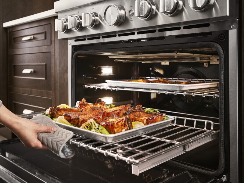 Person pulling a baking tray of roasted meat out of a KitchenAid® oven