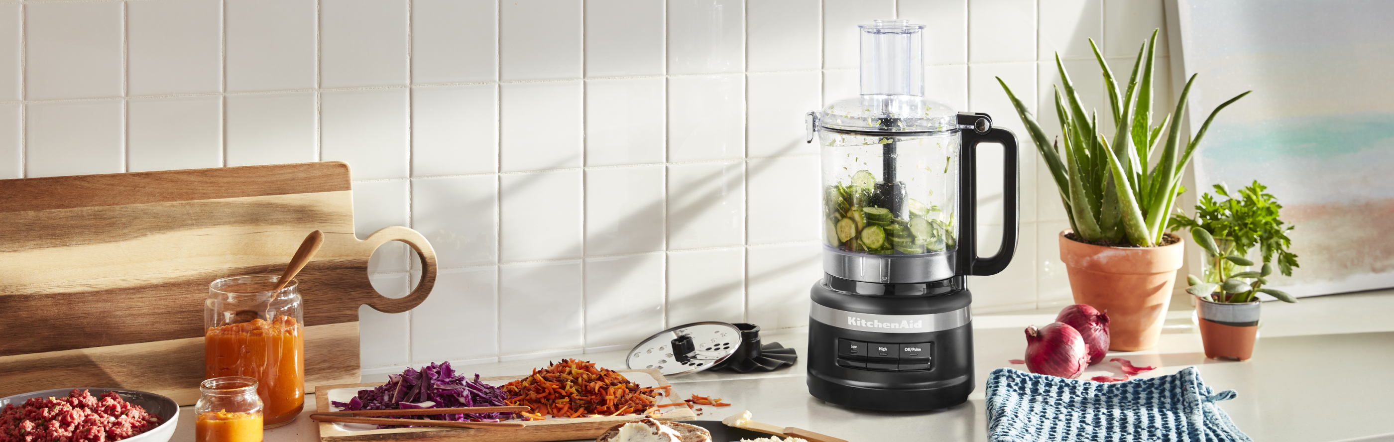 Sliced cucumbers in a KitchenAid® food processor next to shredded vegetables