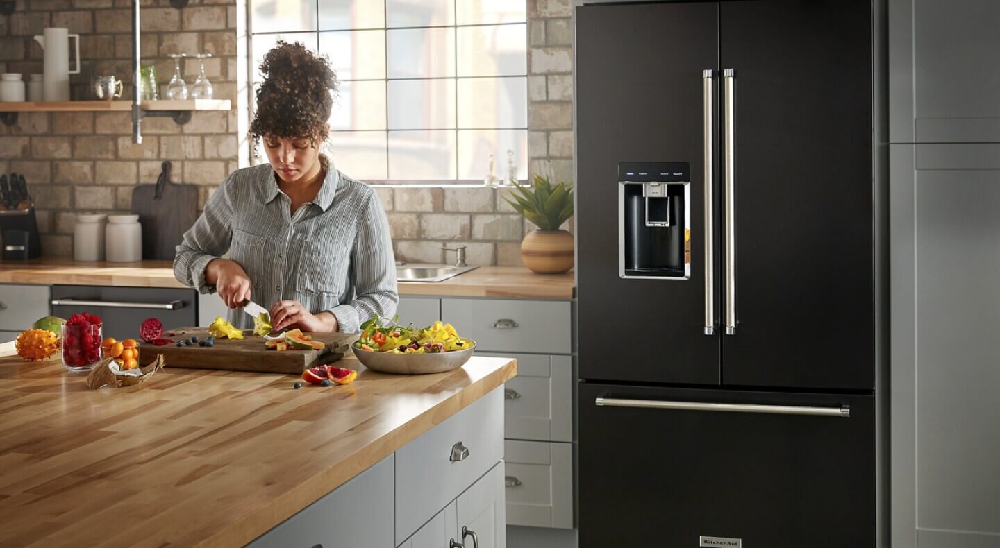 Person preparing food at a kitchen island in front of a black KitchenAid® refrigerator