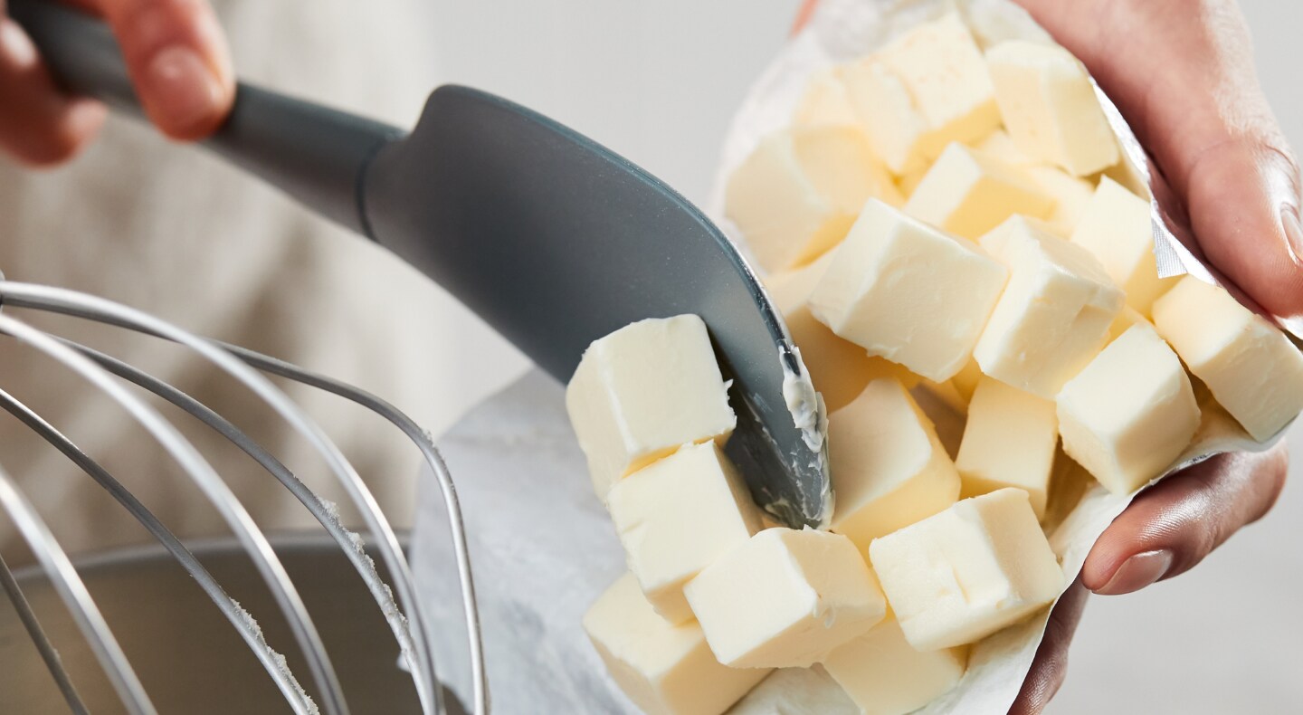 Person using spatula to put slices of butter in a bowl Person using spatula to put slices of butter in a bowl