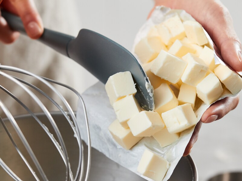 Person using spatula to put slices of butter in a bowl Person using spatula to put slices of butter in a bowl