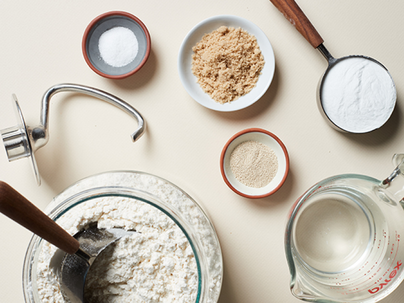 Various ingredients in bowls next to a dough hook accessory