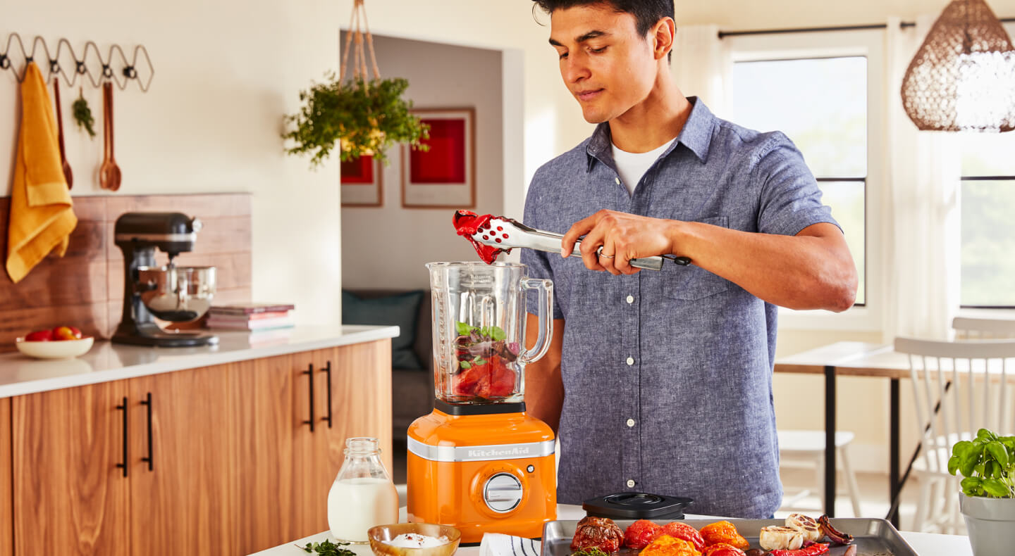 Person adding food to an orange KitchenAid® blender