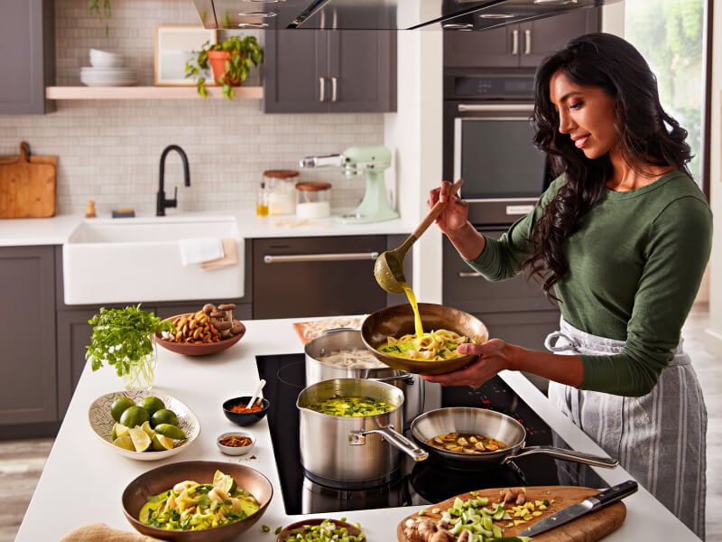 Person pouring broth with a ladle into pan above the cooktop Person pouring broth with a ladle into pan above the cooktop